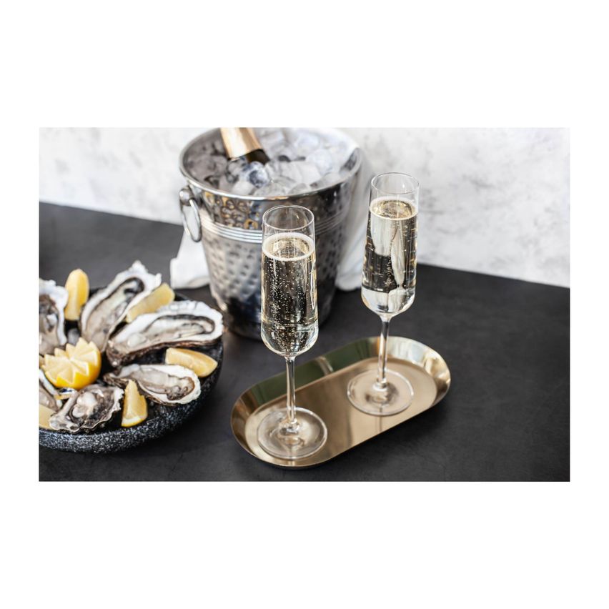 Schaumweingläser mit Luftblasen auf einem Tablett neben einer Muschelschale und einem Eiseimer.