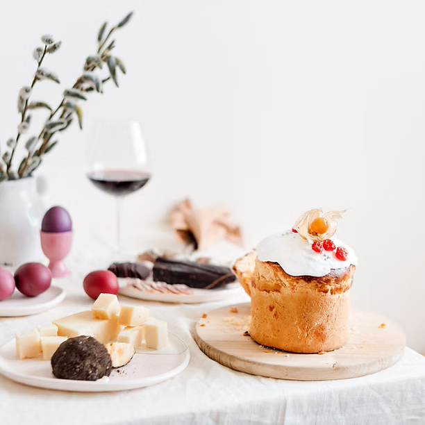 Ein Tisch mit Dessert, Käse, Wein und Ostereiern auf einer weißen Tischdecke.