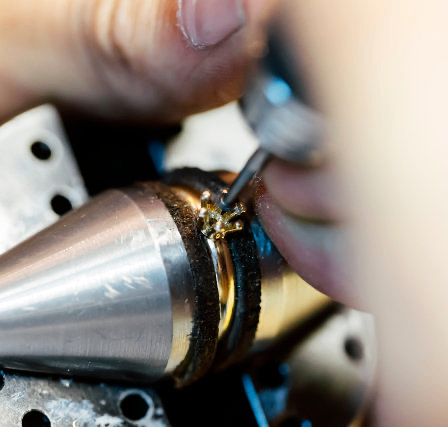 Eine Person, die ein Werkzeug benutzt, um an einem metallischen Objekt zu arbeiten und sich auf ein kleines Goldstück konzentriert.