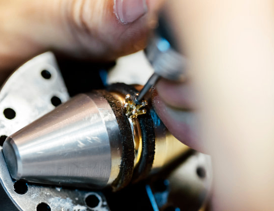 Eine Person, die ein Werkzeug benutzt, um an einem metallischen Objekt zu arbeiten und sich auf ein kleines Goldstück konzentriert.