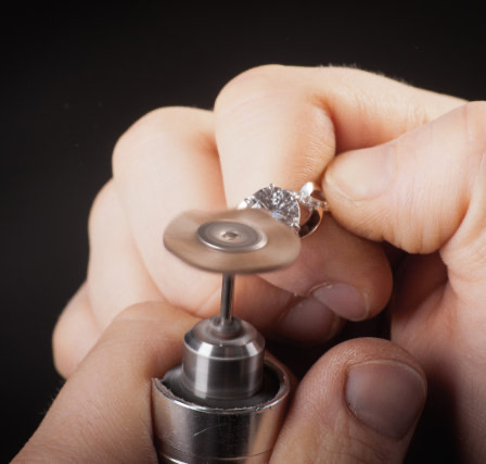 Eine Nahaufnahme der Hände einer Person, die einen Ring hält und mit einem kleinen Metallwerkzeug poliert.