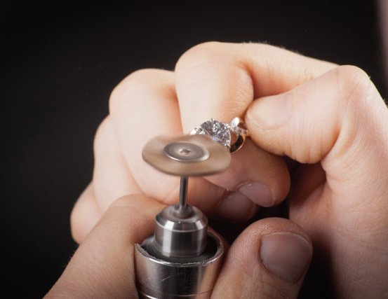 Eine Nahaufnahme der Hände einer Person, die einen Ring hält und mit einem kleinen Metallwerkzeug poliert.