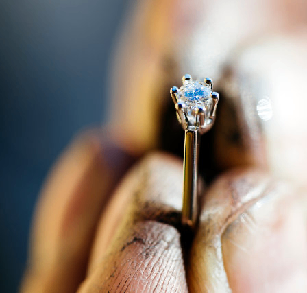 Ein Juwelier untersucht einen Ring mit einem blauen Diamanten, der zwischen zwei Fingern gehalten wird.