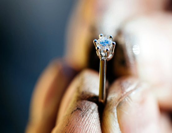 Ein Juwelier untersucht einen Ring mit einem blauen Diamanten, der zwischen zwei Fingern gehalten wird.