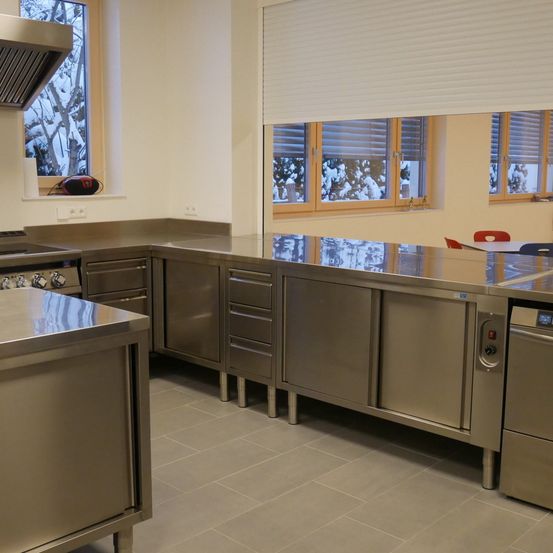 Eine moderne Küche mit Edelstahlgeräten, gefliesten Böden und großen Fenstern mit Jalousien.