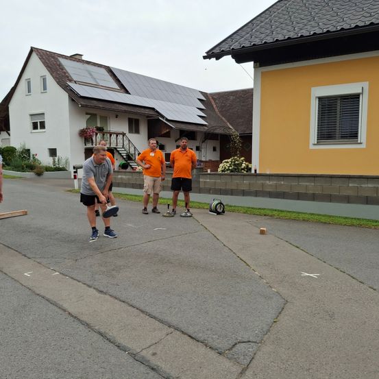 Vier Männer spielen vor einem Haus mit Solarmodulen ein Spiel. Ein Mann hält eine Schläger.