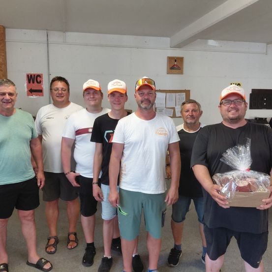 Eine Gruppe von Männern in einem Raum, einer hält eine Box mit Essen, alle tragen Hüte und Freizeitkleidung.