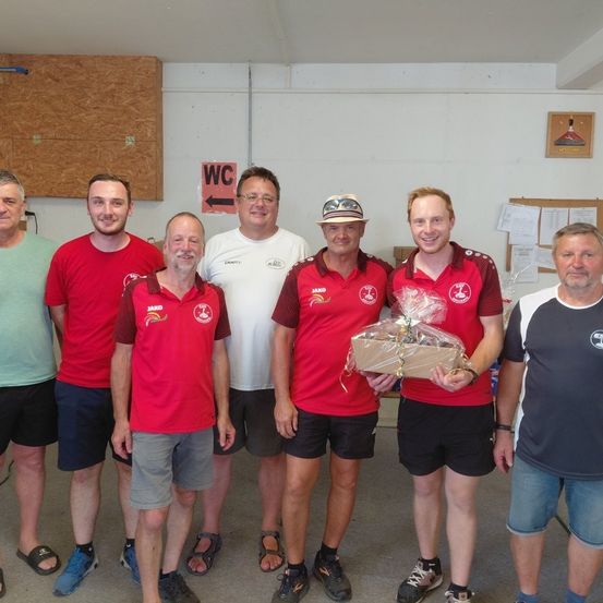 Eine Gruppe von Männern in roten und weißen Hemden und Shorts posiert für ein Foto in einem Raum mit einem Schild, das WC sagt.