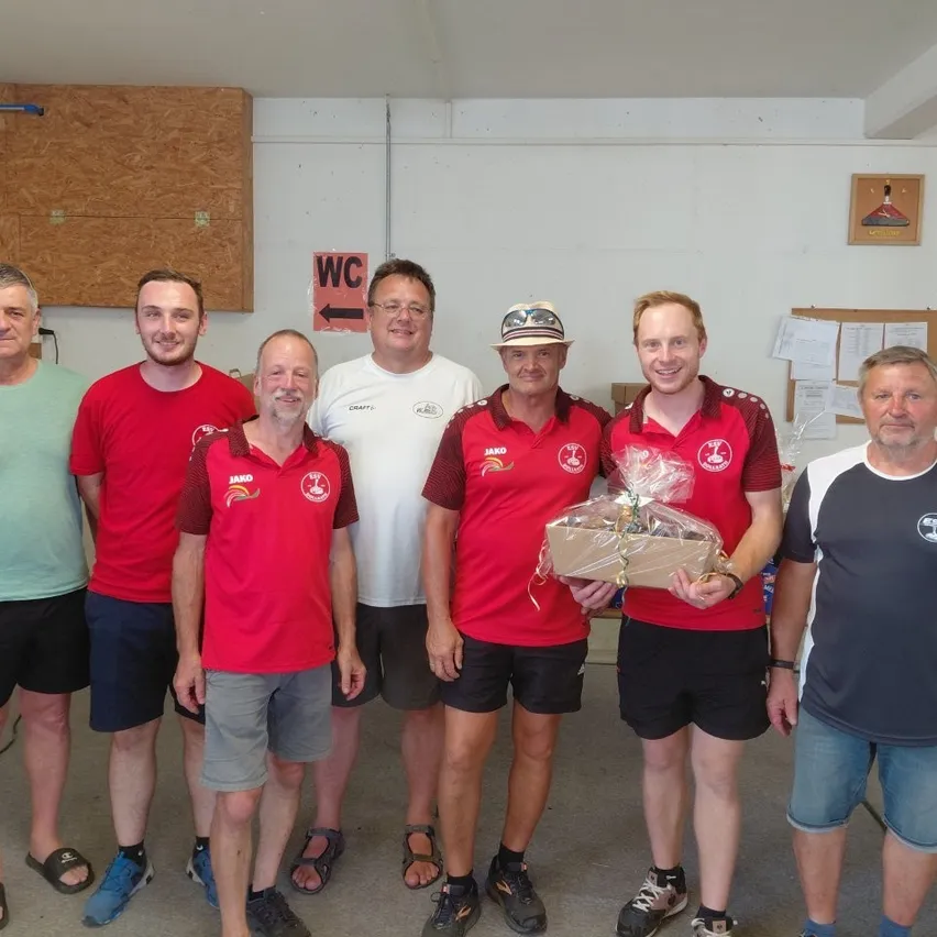 Eine Gruppe von Männern in roten und weißen Hemden und Shorts posiert für ein Foto in einem Raum mit einem Schild, das WC sagt.