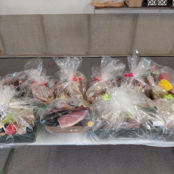 Ein Tisch mit mehreren Plastiktüten, gefüllt mit verschiedenen Lebensmitteln wie Fleisch, Gemüse und Brot, in einer Reihe angeordnet.