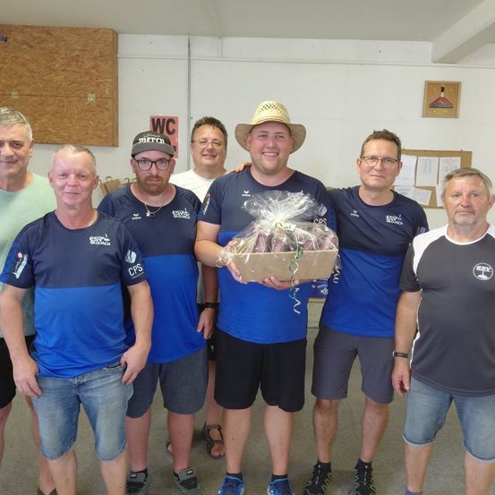Eine Gruppe von Männern in passenden blauen und schwarzen Uniformen steht zusammen, einer hält eine Schachtel mit Obst. Sie scheinen einen Sieg zu feiern.