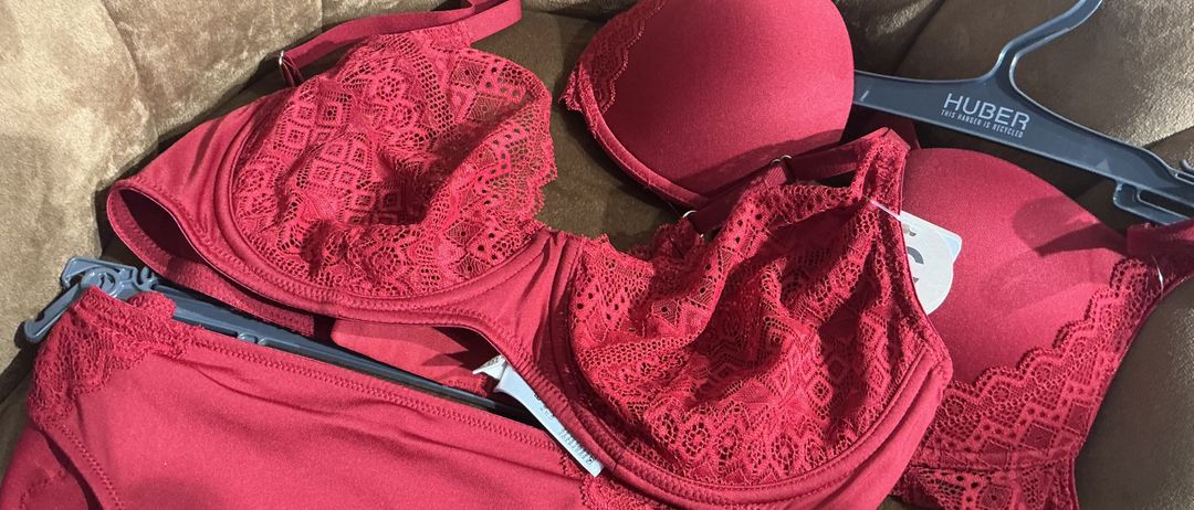 Ein Set roter Spitzen-BHs, einschließlich eines Bralettes und eines BHs, mit einem Kleiderbügel und Etiketten. Der Bralette ist nicht verhakt.