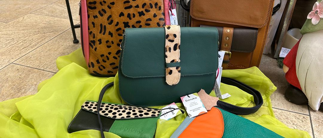 Eine Sammlung von Ledertaschen in verschiedenen Farben und Mustern, einschließlich Leopardenmuster, Punkte und einfarbig, auf einem grünen Tuch präsentiert.