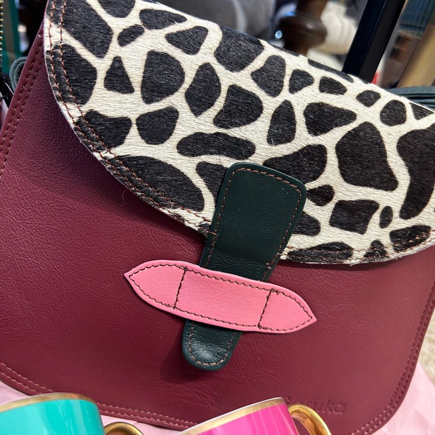A close-up of a red leather handbag with a leopard print flap and pink strap. The bag is placed on a pink surface.