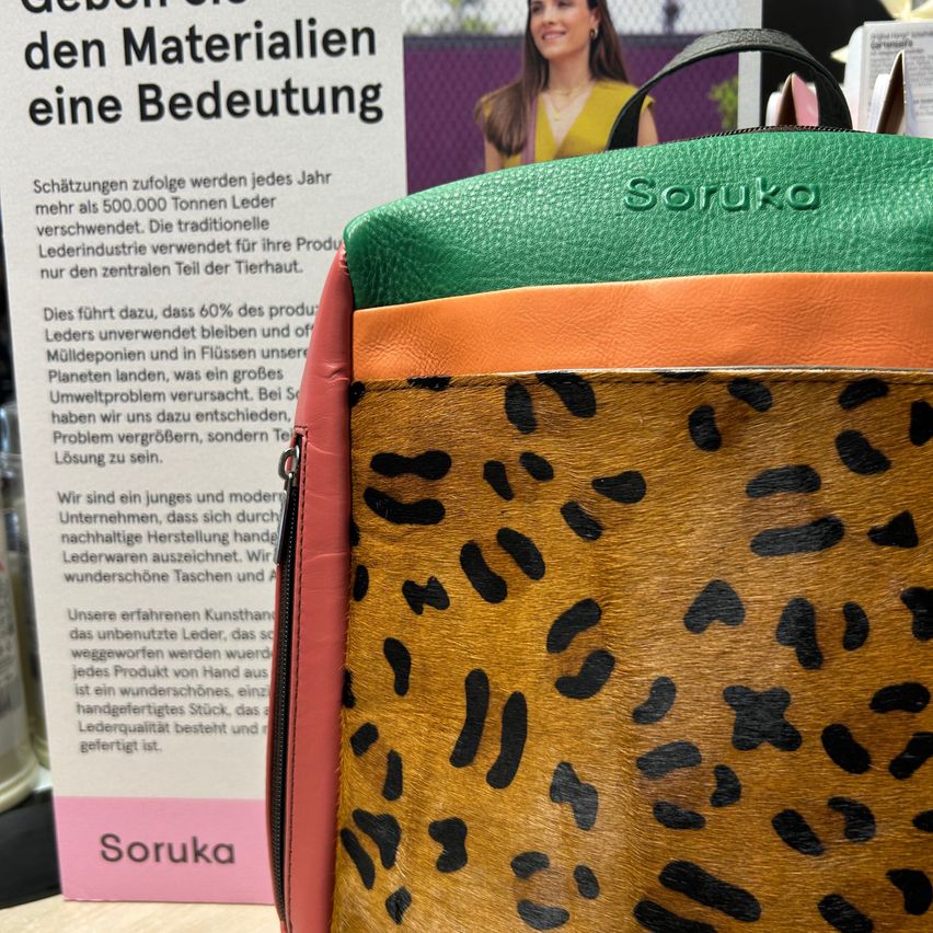 A close up of a leather bag with a leopard print pattern. The bag has a multicolored design. Behind it, there is a sign with German text about the importance of materials.