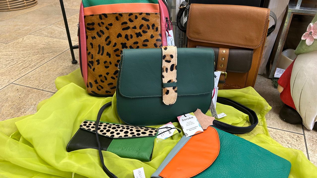 A collection of leather bags in various colors and designs, including leopard print, polka dots, and solid green. Each bag features unique details like straps and tags.