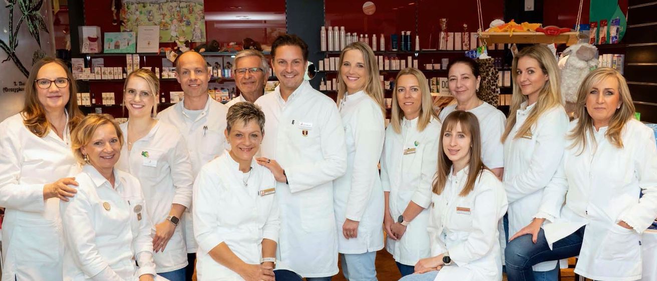 Eine Gruppe von Fachleuten in weißen Kitteln posiert für ein Foto in einem Raum mit Regalen, stehend und sitzend auf Holzkisten.