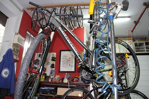 Ein Fahrrad hängt an einem Metallpfosten in einem Raum mit roten Wänden und verschiedenen Gegenständen auf den Regalen.