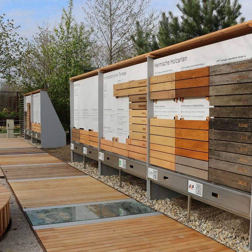 Ein Holzdeck mit einem großen Informationsbrett, das Holzbretter in verschiedenen Farben und Etiketten zeigt. Die Bretter sind auf einer Betonoberfläche platziert.