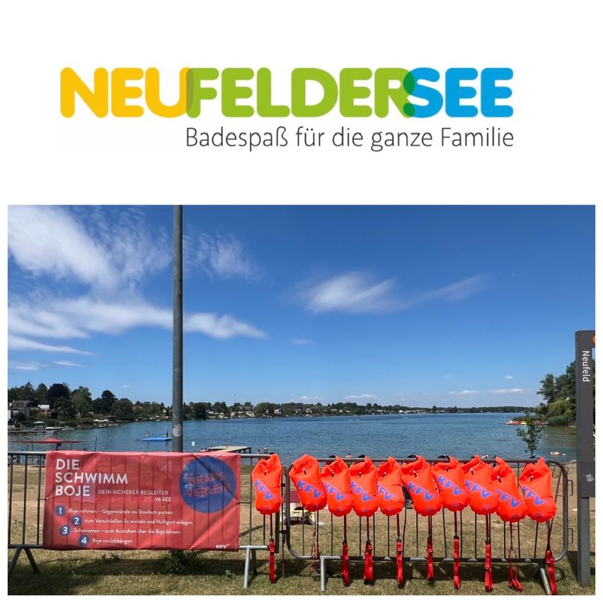 A lake with a clear blue sky and clouds, a banner with safety instructions, and a row of orange life vests hanging on a metal fence.