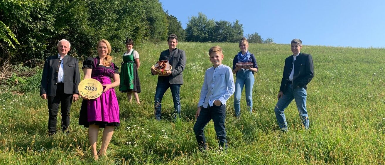 Eine Gruppe von Menschen steht auf einem Grasfeld. Einige halten Trophäen und posieren für ein Foto. Die Frau vorne hält eine Trophäe mit dem Text '2021' und dem Wort 'Längensieger'. Hinter ihr hält ein Mann eine Trophäe.