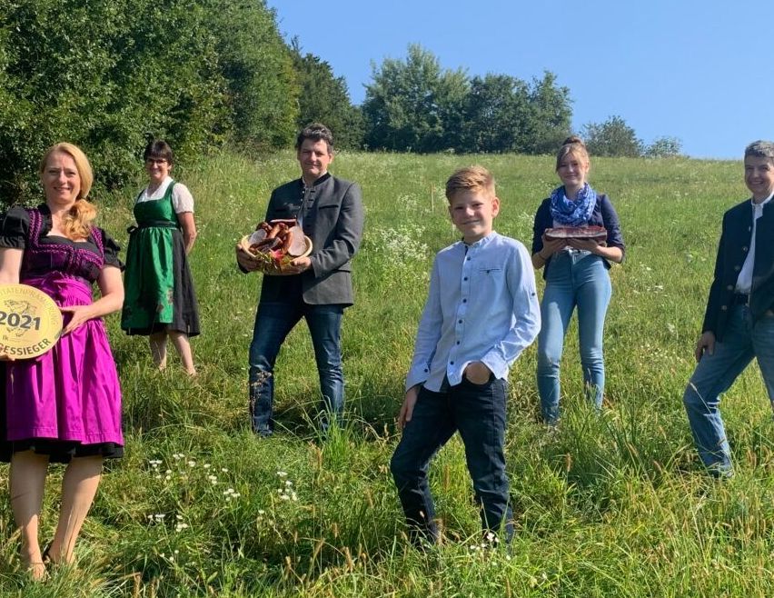 Eine Gruppe von Menschen steht auf einem Grasfeld. Einige halten Trophäen und posieren für ein Foto. Die Frau vorne hält eine Trophäe mit dem Text '2021' und dem Wort 'Längensieger'. Hinter ihr hält ein Mann eine Trophäe.