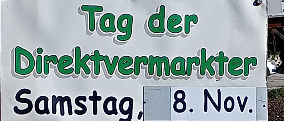 Ein weißer Plakat, das einen Direktmarkt bewirbt. Es zeigt Bilder von Fleisch, Brezen, Marmeladen und Weinen. Der Markt findet am Samstag, dem 8. November, von 9 Uhr bis 13 Uhr statt, veranstaltet von Fam. MENITZ in der Eisenstädter Straße 18, 2485 Wimpassing.