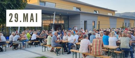 An event poster for Feierabend in Krieglach. Many people sit around tables on a patio. The date is May 29, and the time is 6 PM. The text reads 'Free area of the VAZ'.