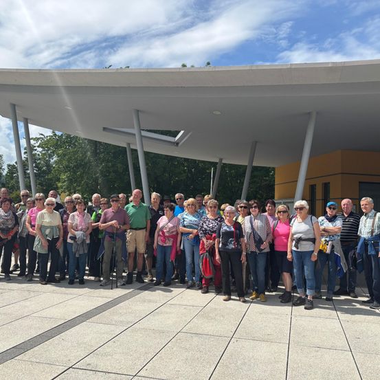 Eine Gruppe von Menschen, wahrscheinlich Touristen, steht unter einem Vordach auf einem Betonboden und lächelt und posiert für ein Foto.