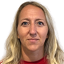 Eine Frau mit blonden Haaren, die ein rotes Rollkragenshirt trägt, sieht mit einem neutralen Gesichtsausdruck direkt in die Kamera.