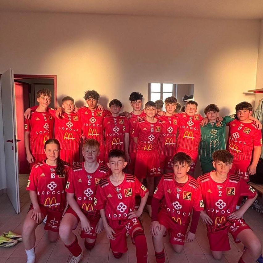 Eine Gruppe junger Fußballspieler in roten Trikots mit McDonald's-Logo posiert für ein Foto in einem Raum. Sie knien oder stehen und bilden einen Halbkreis.