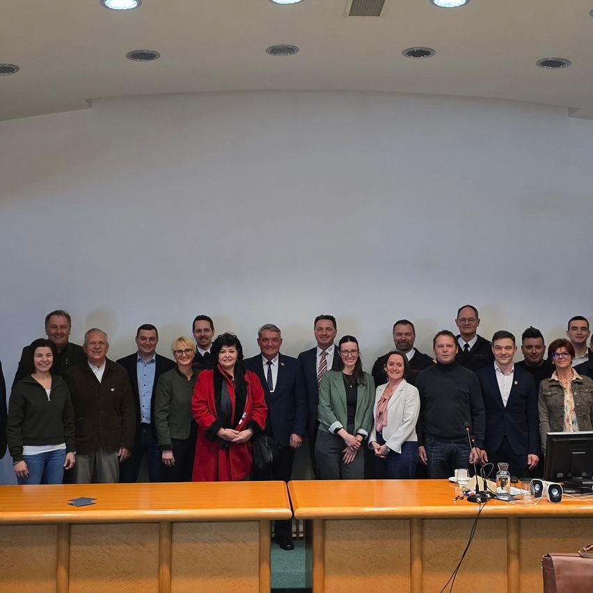 Eine Gruppe von Personen, die formell gekleidet sind, steht in einem Konferenzraum, lächelt und posiert für ein Foto.