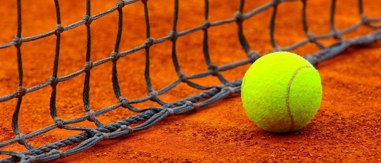 Ein Tennisplatz mit einem gelben Tennisball, der neben einem Netz auf dem Boden ruht.