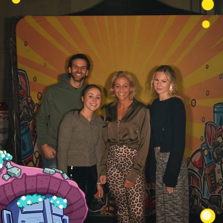 Vier Menschen stehen vor einem farbenfrohen Hintergrund. Sie scheinen alle zu lächeln und posieren für ein Foto.