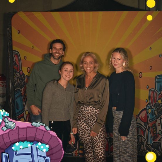 Vier Menschen stehen vor einem farbenfrohen Hintergrund. Sie scheinen alle zu lächeln und posieren für ein Foto.