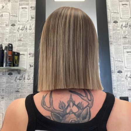 Eine Frau mit kurzem, blondem Haarschnitt steht in einem Salon. Sie hat ein Hirsch-Tattoo auf dem Rücken.