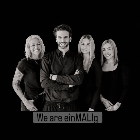 Ein schwarz-weißes Bild von vier Menschen, die zusammenstehen und lächeln, wobei der Mann in der Mitte steht und unten die Worte 'Wir sind einMALig' stehen.