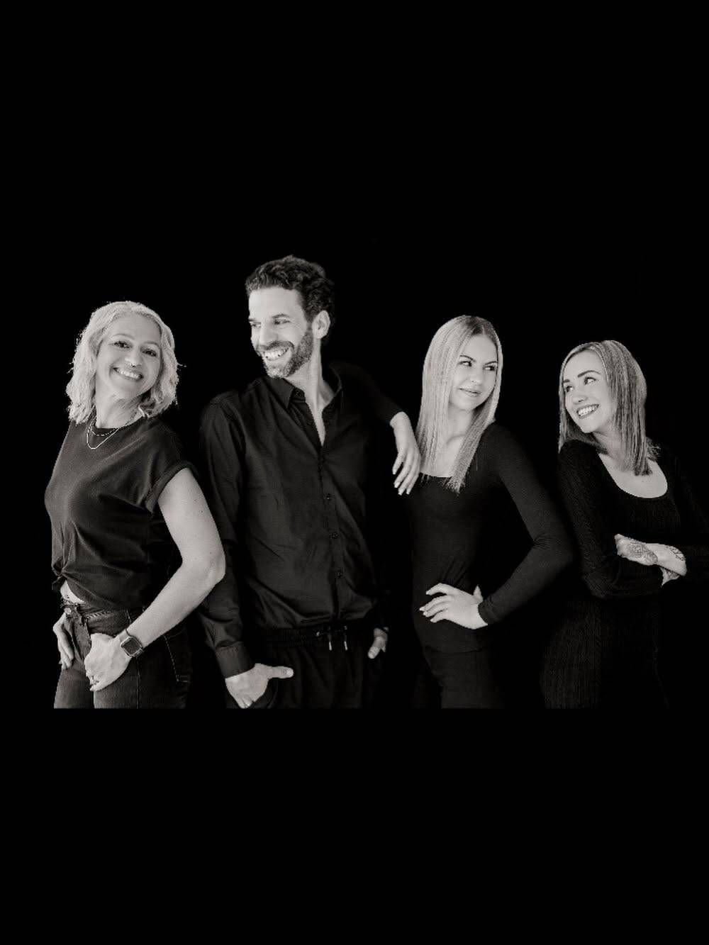 Ein Schwarz-Weiß-Foto von vier lächelnden Personen, zwei Frauen an den Seiten und einem Mann in der Mitte.