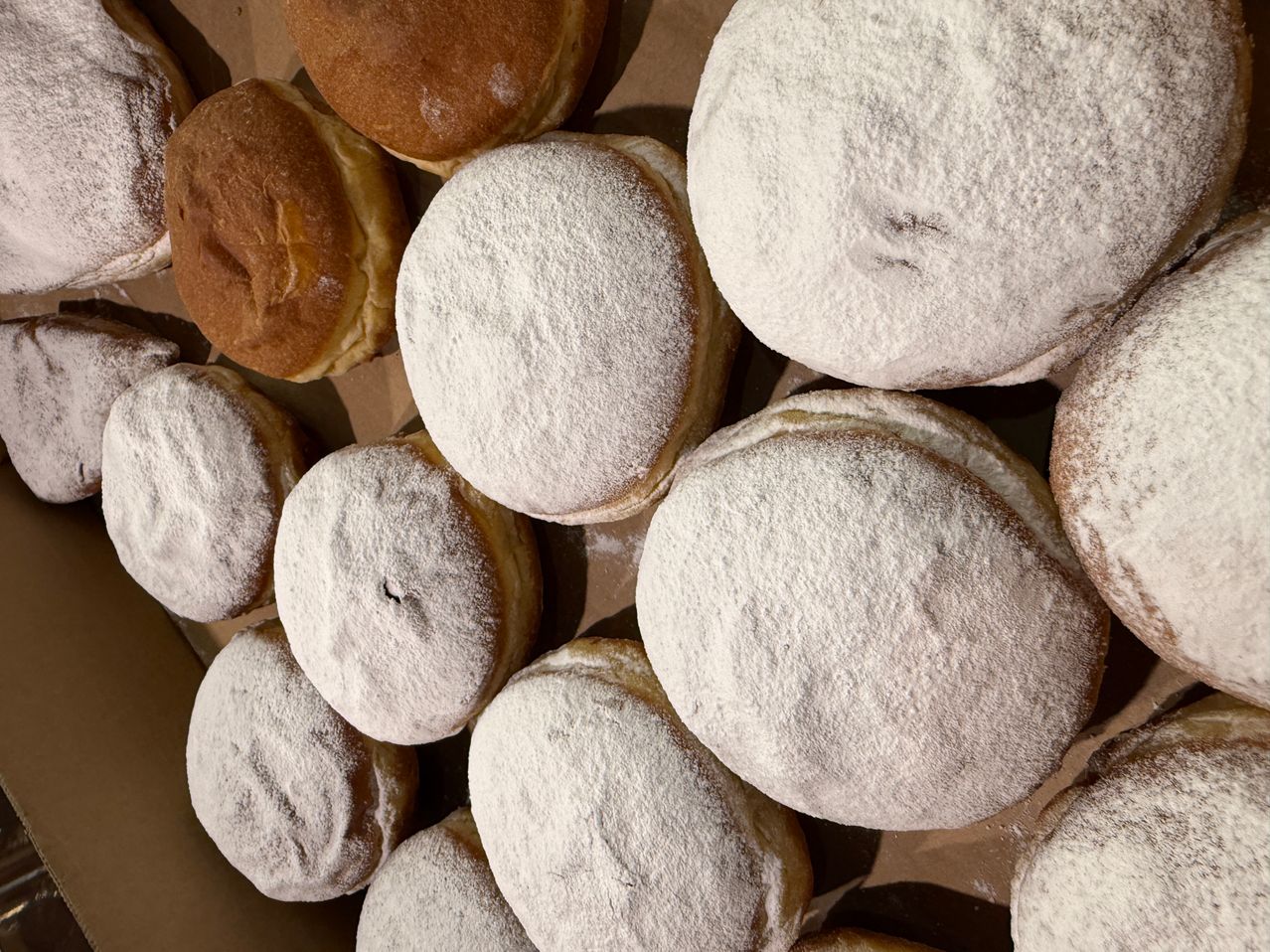 Eine Nahaufnahme von mehreren runden Gebäckstücken, einige mit Puderzucker bestreut und andere glasiert, in einem braunen Papierbeutel angeordnet.