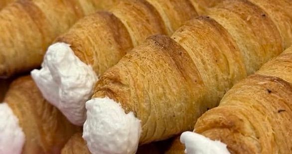 Eine Nahaufnahme von mehreren Croissants, goldbraun und blättrig, mit Schlagsahne obenauf, die ihre Textur und ihren Duft hervorhebt.