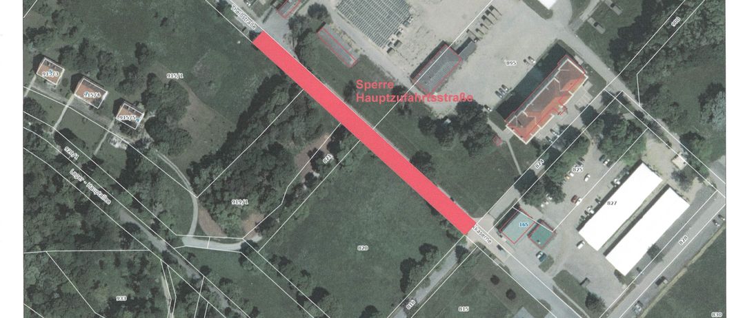 Eine Luftaufnahme eines Vorstadtgebiets zeigt eine Hauptstraße, die als Sperre Hauptzufahrtsstraße beschriftet ist. Die Karte enthält einen Maßstab und Entfernungsanzeigen. Es gibt Gebäude, Bäume und einen Parkplatz. Das Gebiet ist von Grün umgeben und umfasst andere Straßen und einen Parkplatz.