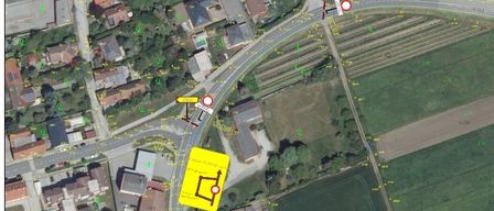 Aerial view of a town with several houses and a road. A yellow sign with a circular arrow points to the right. A red sign is also present.