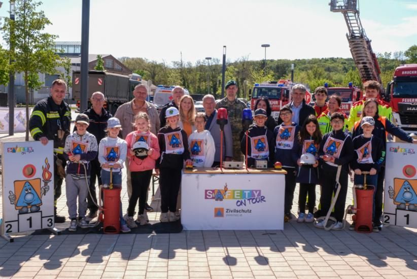 Eine Gruppe von Menschen, darunter Kinder, steht vor einem Tisch mit einem Schild, das Sicherheitstour sagt, umgeben von Feuerwehrwagen und Feuerwehrleuten.