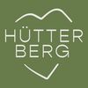 Das Logo für Hutterberg auf grünem Hintergrund, mit einem stilisierten Berg und einem Herz mit lächelndem Gesicht.