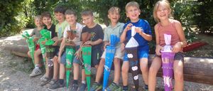 A group of children holding decorated bags, smiling and sitting on a bench in an outdoor area.