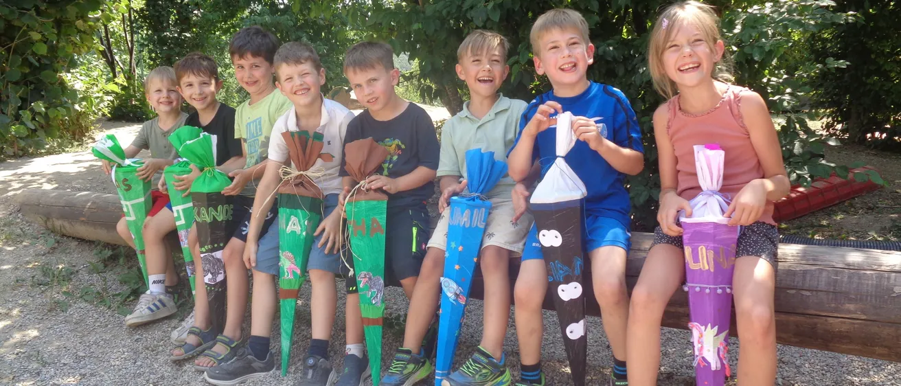Eine Gruppe von Kindern, die dekorierte Tüten halten, lächelnd auf einer Bank in einem Außenbereich sitzend.