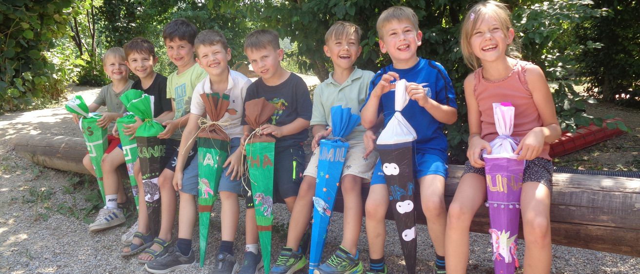 Eine Gruppe von Kindern, die dekorierte Tüten halten, lächelnd auf einer Bank in einem Außenbereich sitzend.