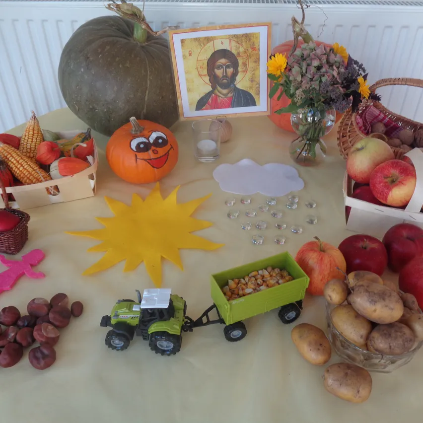 Ein Tisch mit verschiedenen Herbstartikeln, einschließlich Kürbisse, Äpfel, Mais und ein Bild von Jesus.