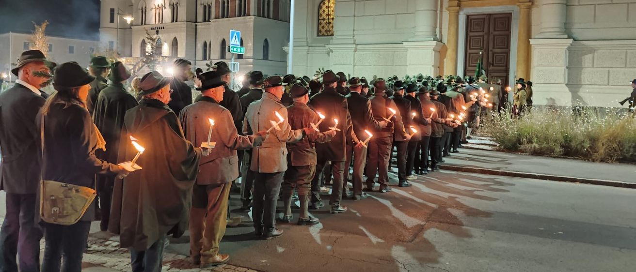 Eine Reihe von Männern in Hüten mit brennenden Kerzen steht nachts vor einer Kirche.