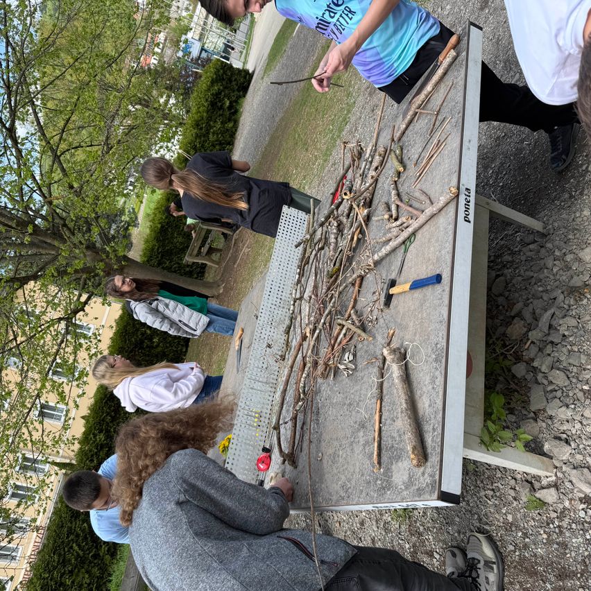 Eine Gruppe von Menschen in einem Park arbeitet an einem Projekt mit Zweigen und Werkzeugen auf einem Tisch.